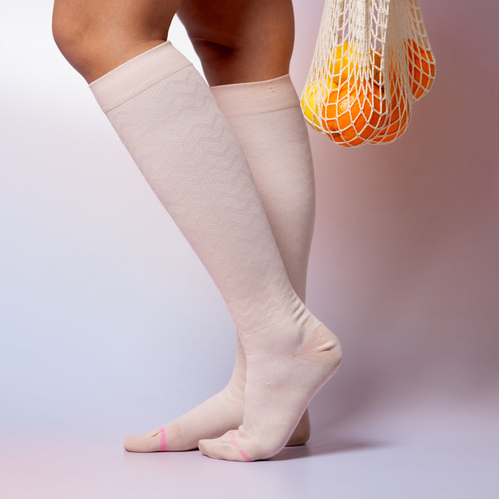 Knee-high compression socks with a chevron pattern, worn by a person holding a mesh bag with oranges.