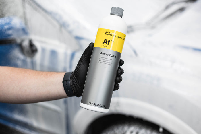 Person holding a bottle of 'Active Foam' car wash product with a blurred car in the background