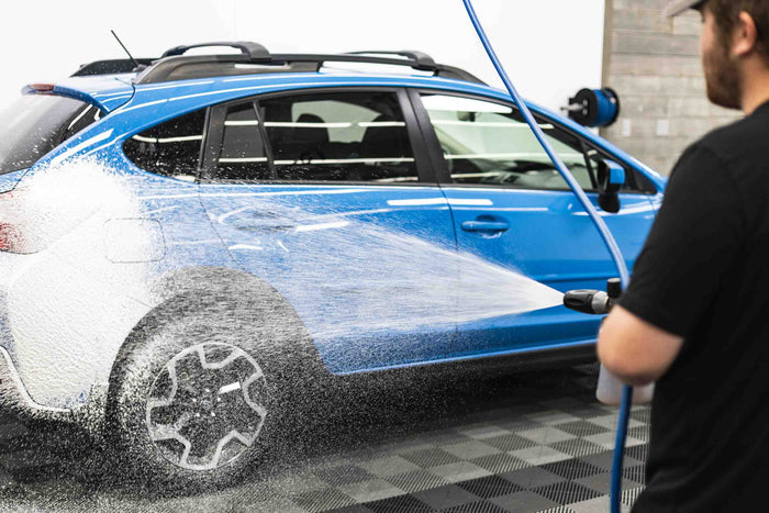 A person washing a blue car with an iK foam sprayer filled with KochChemie Active Foam.