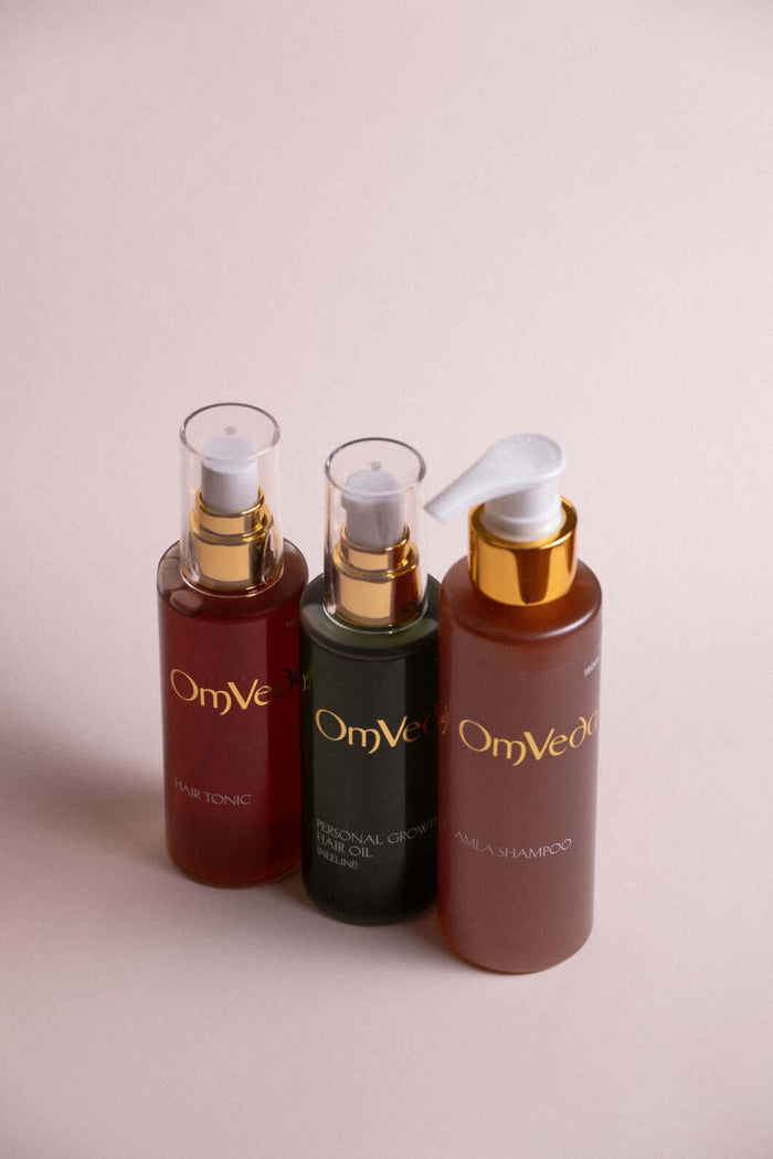 Ayurvedic hair care bundle: three pump bottles, OmVe label, amber and brown tones