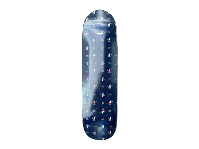 A skateboard deck with a dark blue background and a repeating white pattern of small boats, photographed vertically against a gray tiled floor.
