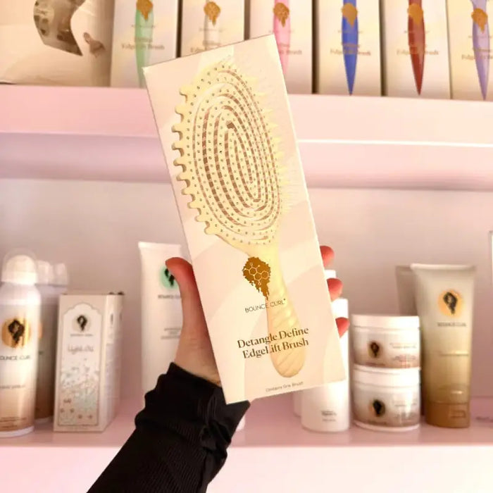 Bounce Curl Detangle Define EdgeLift Brush for curly hair care, held in hand with product shelves in background