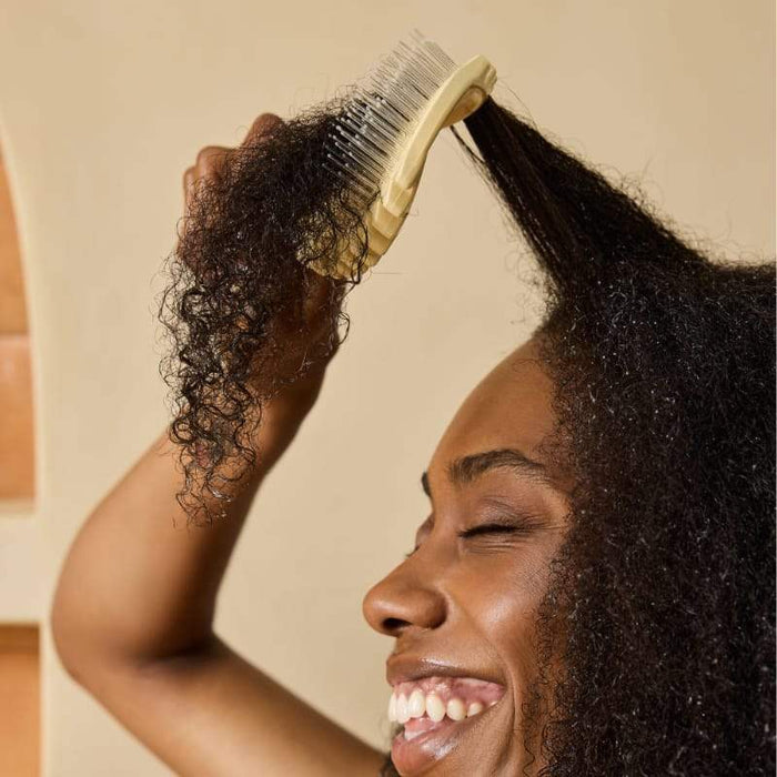 Woman brushing curly hair with wide-tooth detangling brush for healthy curls