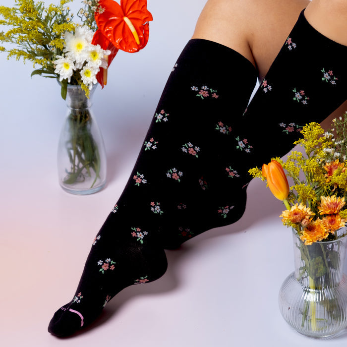 Knee-high black compression socks with a ditsy floral pattern, paired with colorful flower arrangements.