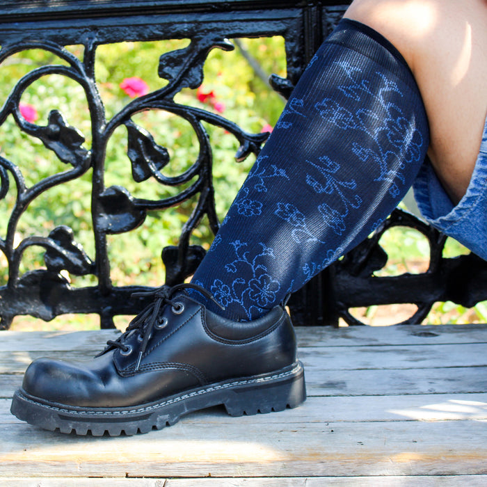 Knee-high compression socks with a floral pattern, worn with a black shoe, resting on a wooden surface.