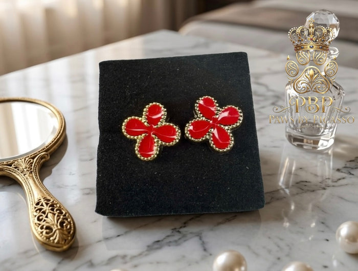 Red floral earrings on a black stand with a perfume bottle and mirror in the background.