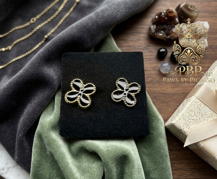Clover-shaped earrings on a black stand with 'Paws by Picasso' branding, surrounded by decorative items.