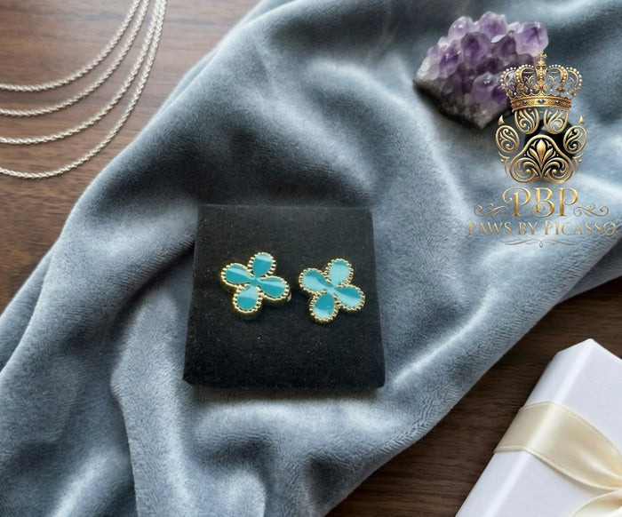 Turquoise flower-shaped earrings on a black stand with gray fabric and amethyst stone in the background, branded 'Paws by Picasso