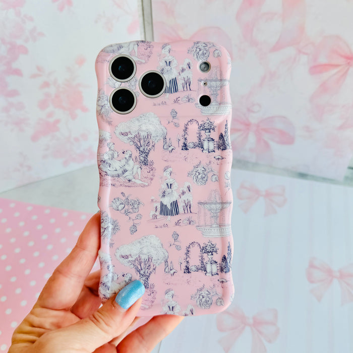 Hand holding the French Affair Wavy Luxe MagSafe iPhone case, showing the soft pink toile print with pastoral scenes in fine grey linework.