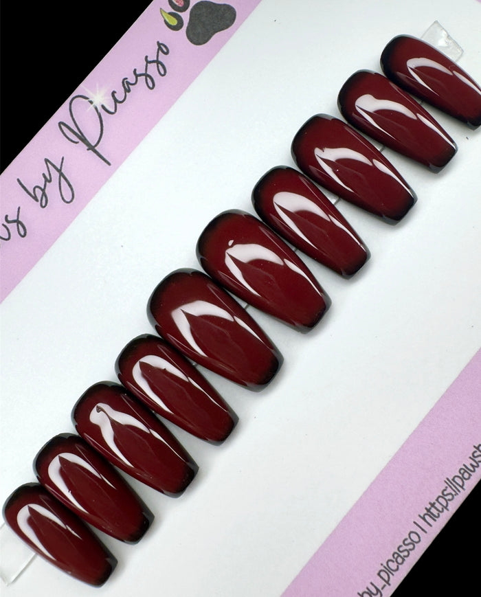 Set of dark red nails on a white and pink background with 'Paws by Picasso' branding.