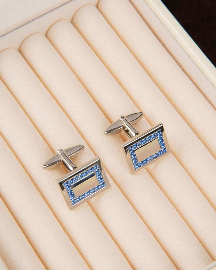 Rectangular blue crystal cufflinks with silver frame on beige display cushion