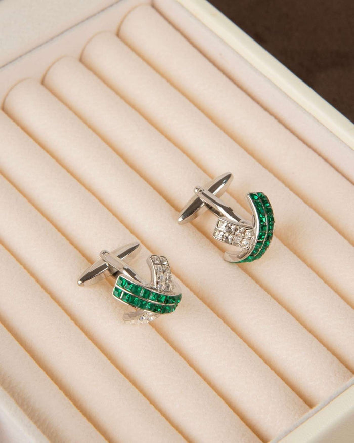Silver cufflinks with green crystal wave design and clear stone accents on display