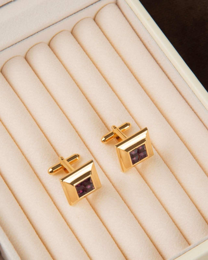 Gold tone square cufflinks with purple crystal square centers on display tray