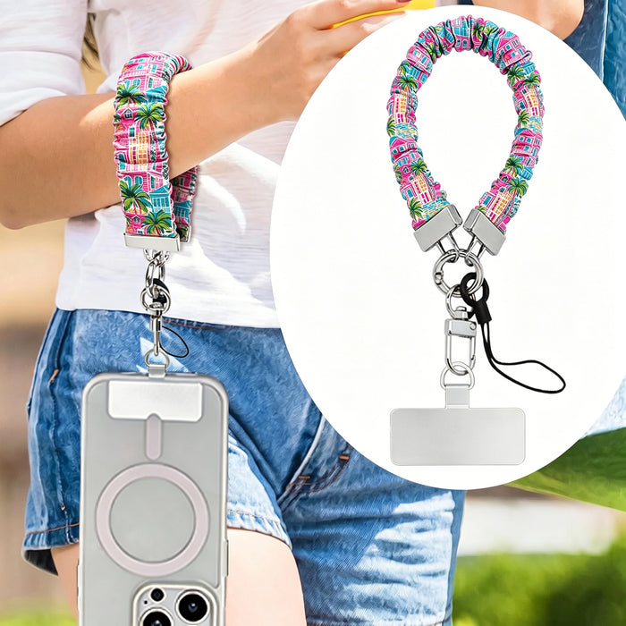 A stretchy scrunchie-style phone wrist strap with a metal clasp and phone tether tab, shown worn on the wrist and attached to a phone.