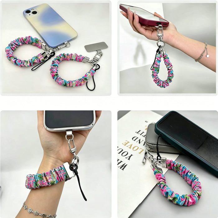 A stretchy scrunchie-style phone wrist strap with a metal clasp and phone tether tab, shown worn on the wrist and attached to a phone.