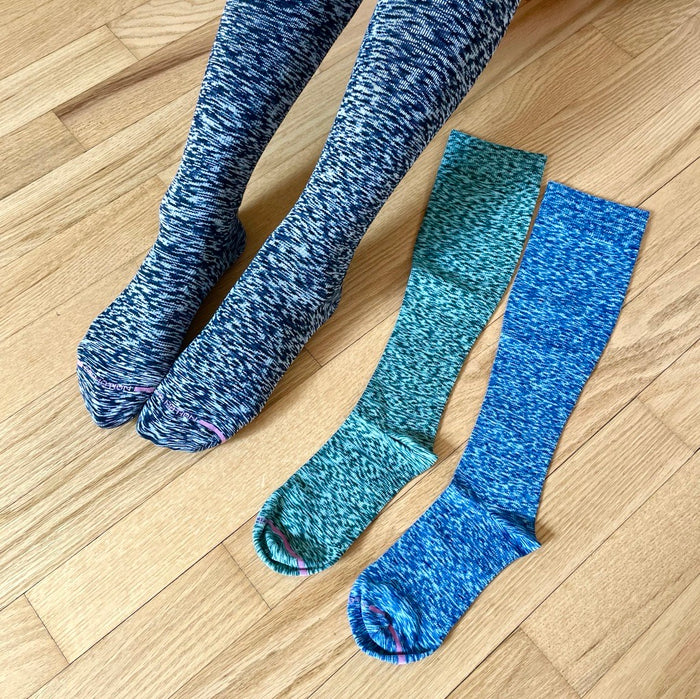 Knee-high compression socks in blue and teal colors, displayed on a wooden floor.