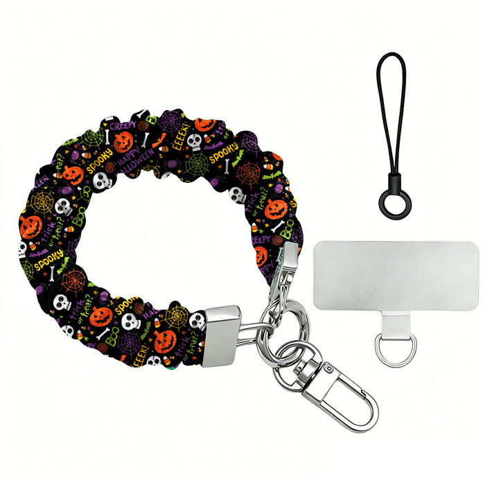 Spooky scrunchie phone wrist strap shown with its metal clasp and phone attachment tab, black fabric printed with pumpkins, skulls and spiderwebs.