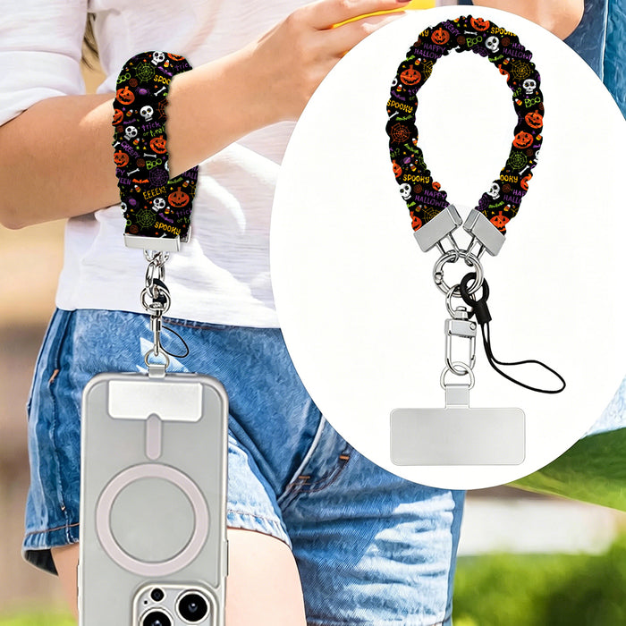 Spooky scrunchie phone wrist strap worn on the wrist and clipped at the hip, with a close-up of the black pumpkin and skull print.