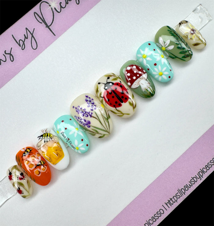 Decorative nail art with flowers, ladybugs, and mushrooms on a white background.