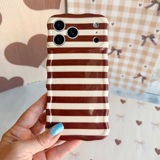 Hand holding the Sweet Espresso Stripes Wavy Luxe MagSafe iPhone case, showing the espresso brown and cream stripes against a tan gingham and bow backdrop.
