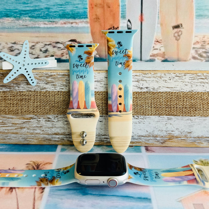 Sweet Summer silicone Apple Watch band with pastel pink, yellow, and blue surfboards, palm trees, and "sweet summer time" script on a soft watercolor beach scene, shown displayed and worn on Apple Watch against a coastal surfboard backdrop.