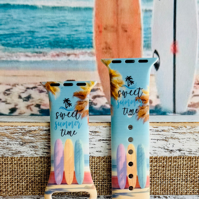 Sweet Summer silicone Apple Watch band with pastel pink, yellow, and blue surfboards, palm trees, and "sweet summer time" script on a soft watercolor beach scene, shown displayed and worn on Apple Watch against a coastal surfboard backdrop.