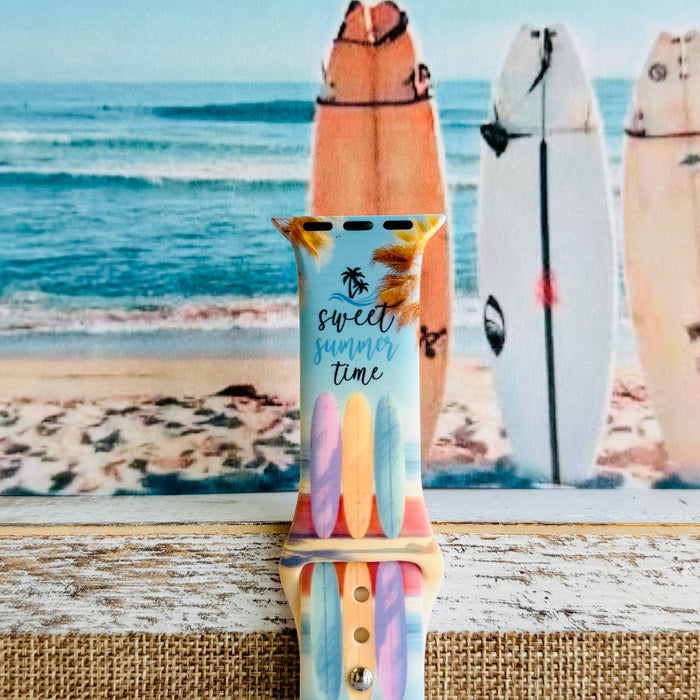 Sweet Summer silicone Apple Watch band with pastel pink, yellow, and blue surfboards, palm trees, and "sweet summer time" script on a soft watercolor beach scene, shown displayed and worn on Apple Watch against a coastal surfboard backdrop.