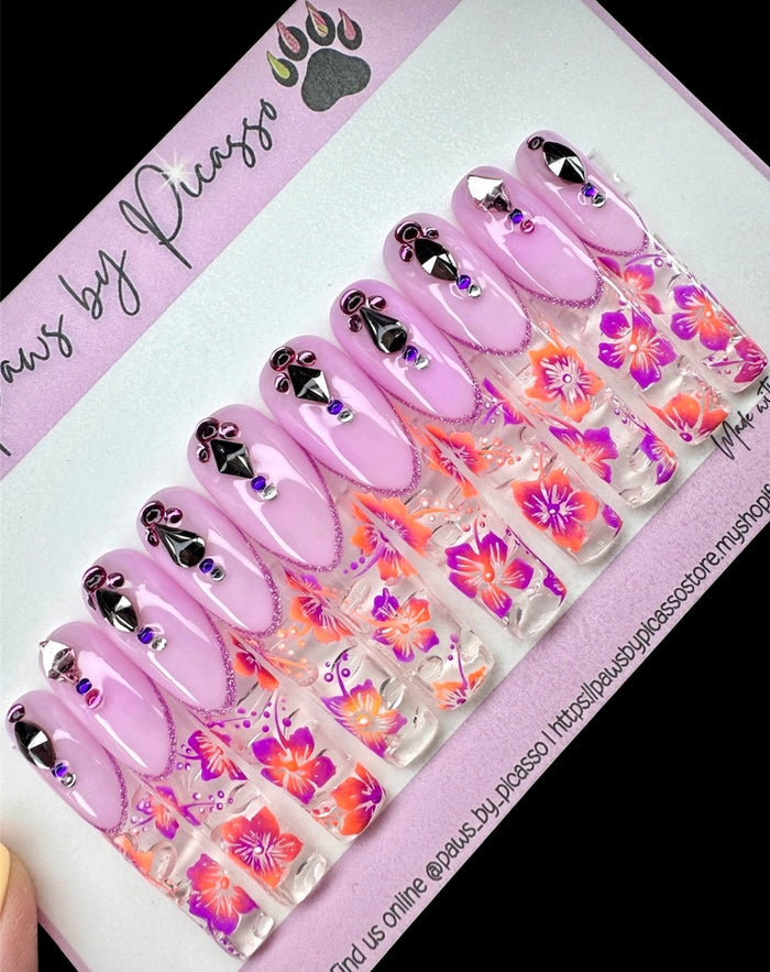 Set of purple nail art designs with floral patterns on a branded packaging.