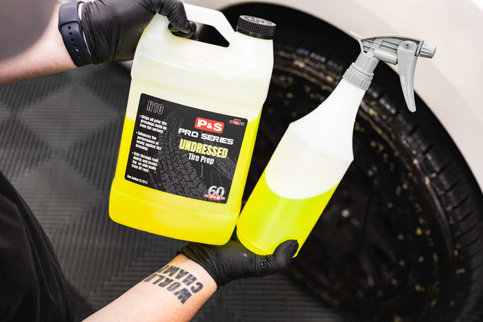 A Jug and spray bottle of P&S Undressed held by a person with gloves against a car tire background.
